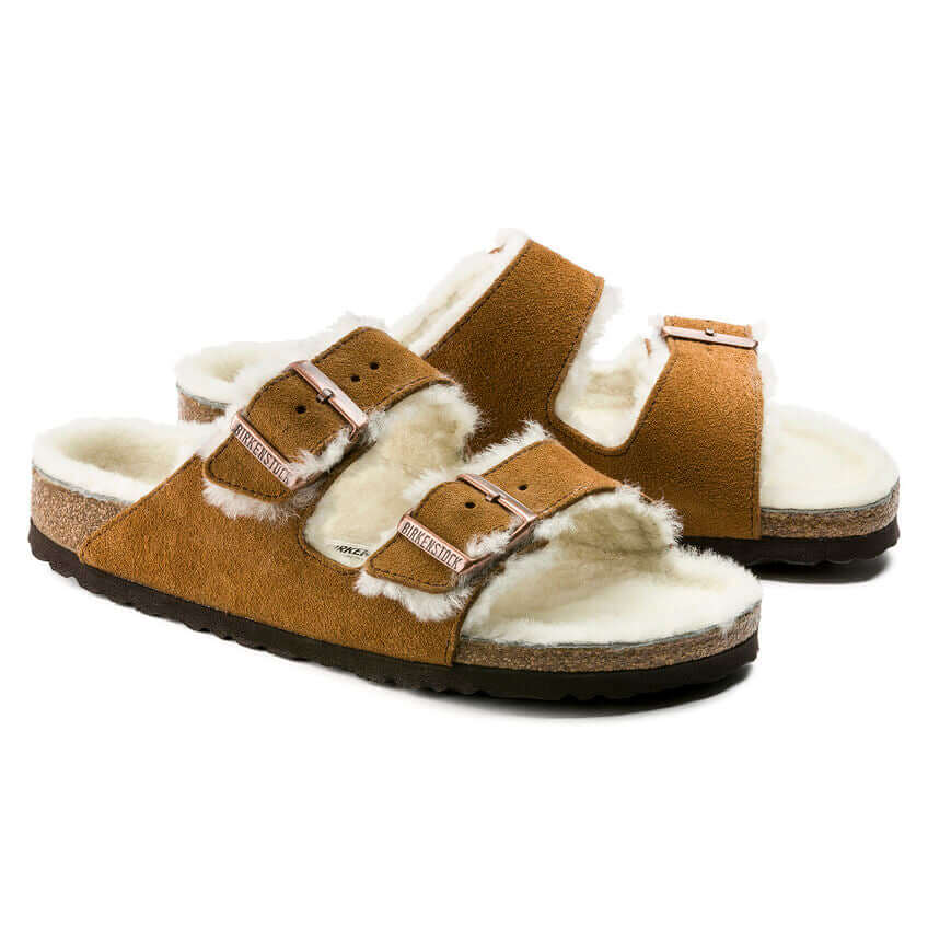 Brown shearling-lined sandals with double buckle straps on a cork sole.