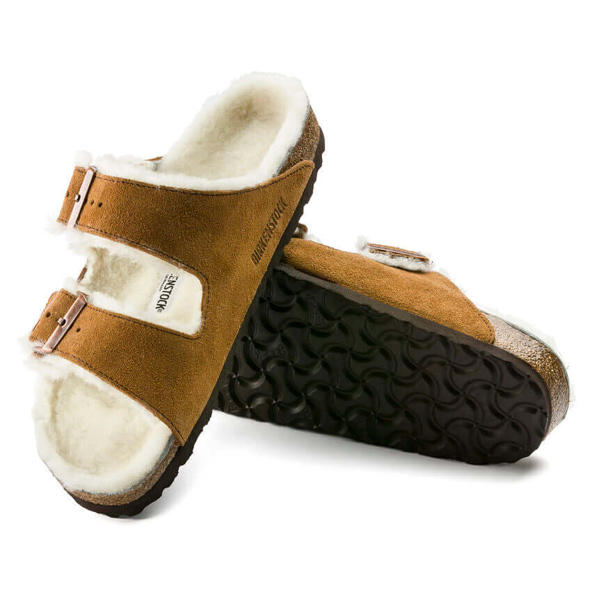 Brown Birkenstock shearling lined sandals with white fur, double buckle straps, and black rubber soles, shown in a pair.