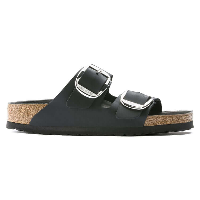 Black two-strap sandal with cork footbed and metallic buckles on white background.